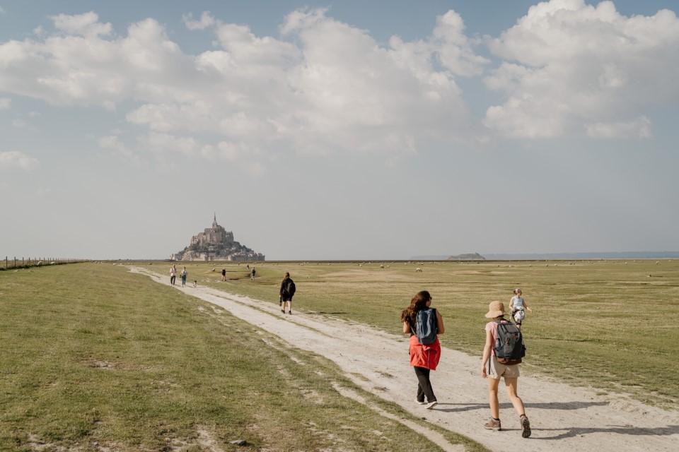 arrivee-mont-saint-michel-emilie-ursule Randonneurs marchant vers le Mont-Saint-Michel, emblème de la Normandie.