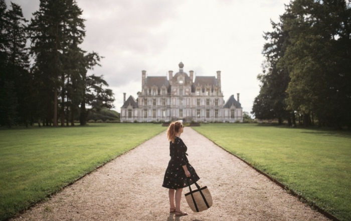Femme face au château de Beaumesnil avec un sac en osier.