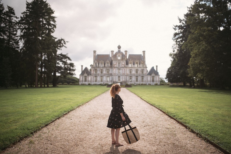 chateau-de-beaumesnil-femme-valise-credit-miles-et-love Femme face au château de Beaumesnil avec un sac en osier.