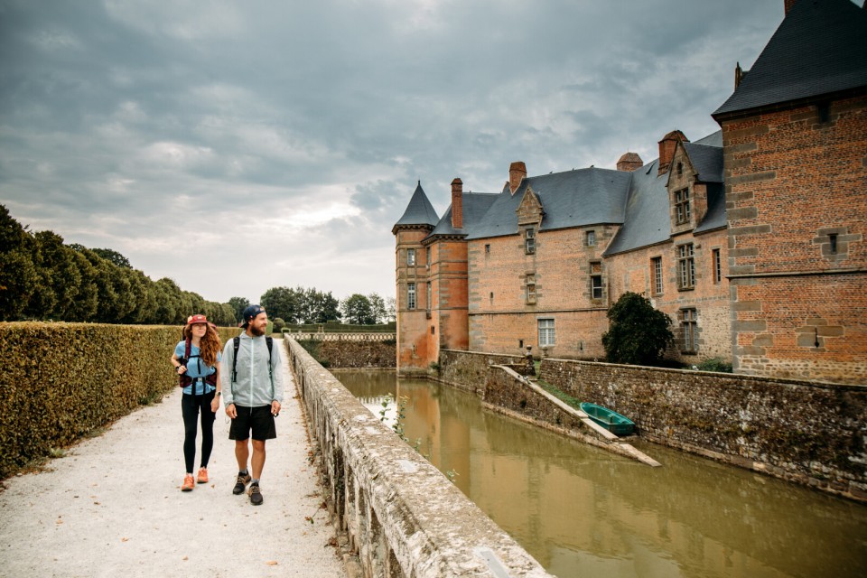 chateau-de-carrouges-randonneurs-credit-amelie-blondiaux Deux randonneurs passent devant les douves du château de Carrouges.