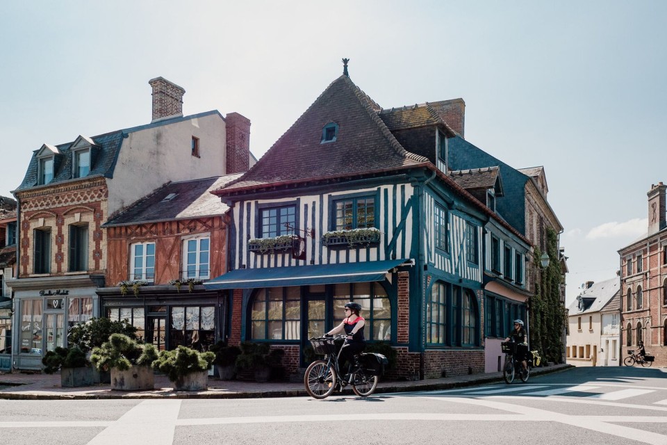 cyclotourisme-beaumont-en-auge-calvados-thomas-le-floc-h Cyclistes passant devant des maisons à colombages à Beaumont-en-Auge.